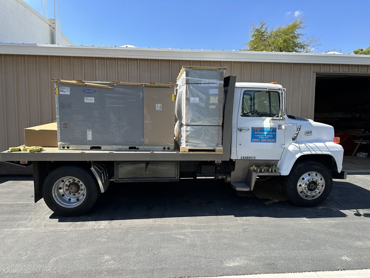 JP Air Conditioning flatbed truck delivering a new HVAC unit